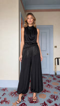 Front view of model wearing black satin cowl neck fringe jumpsuit
